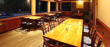 A restaurant with wooden tables and chairs, large windows, and brick walls.