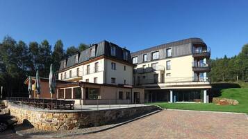 A multi-story hotel with a stone facade, outdoor seating area, and a paved walkway.