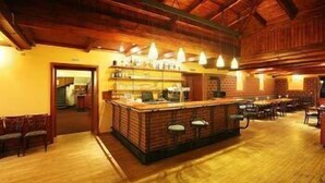 A rustic bar area with wooden flooring and a brick counter, surrounded by tables and chairs. - Hotel Ostrov (Tisa)