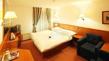 Une chambre d’hôtel comprenant un lit, une table de chevet, une lampe, une chaise et une petite table sur laquelle se trouve un plateau avec divers objets.