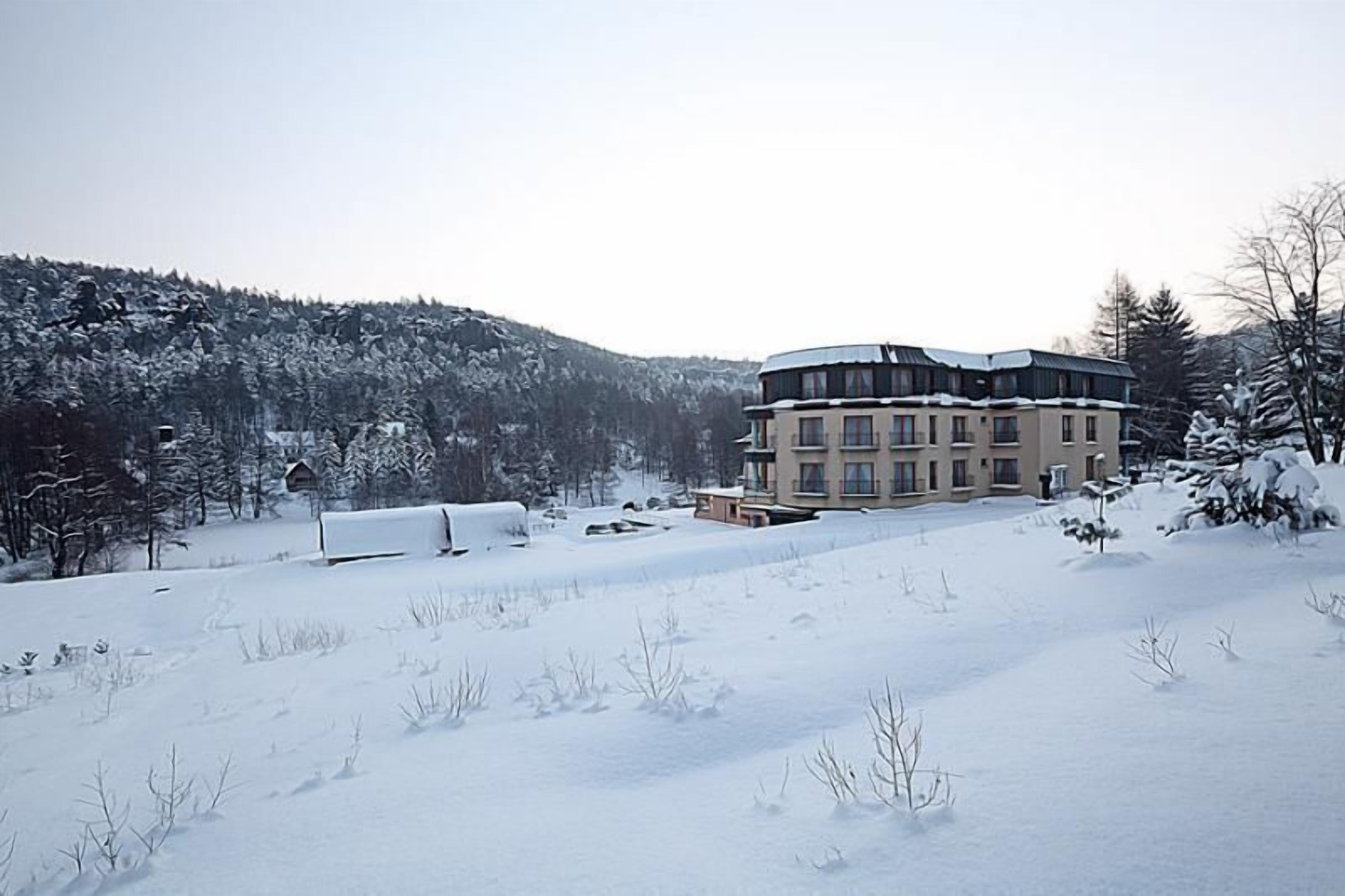 A multi-story building with a flat roof, surrounded by snow-covered landscape and trees.