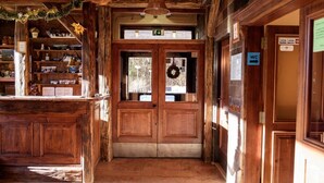 Un interior de madera con una mesa de recepción, un doble puerta adornada con un adorno festivo y un letrero que señala un baño.