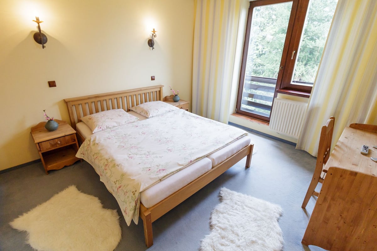 Ein Schlafzimmer mit einem hölzernen Bett, zwei Nachttischen, einem Schminktisch, einem weißen, flauschigen Teppich, einer Holzkommode und einem Fenster mit Vorhängen.