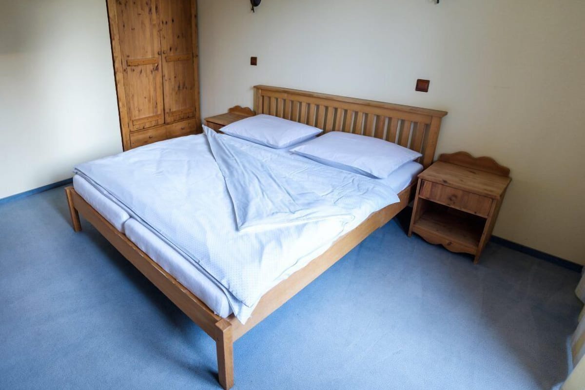 Ein Einzelbett mit Holzbettrahmen und blauer Matratze, ein Nachttisch aus Holz und ein Holzschrank.