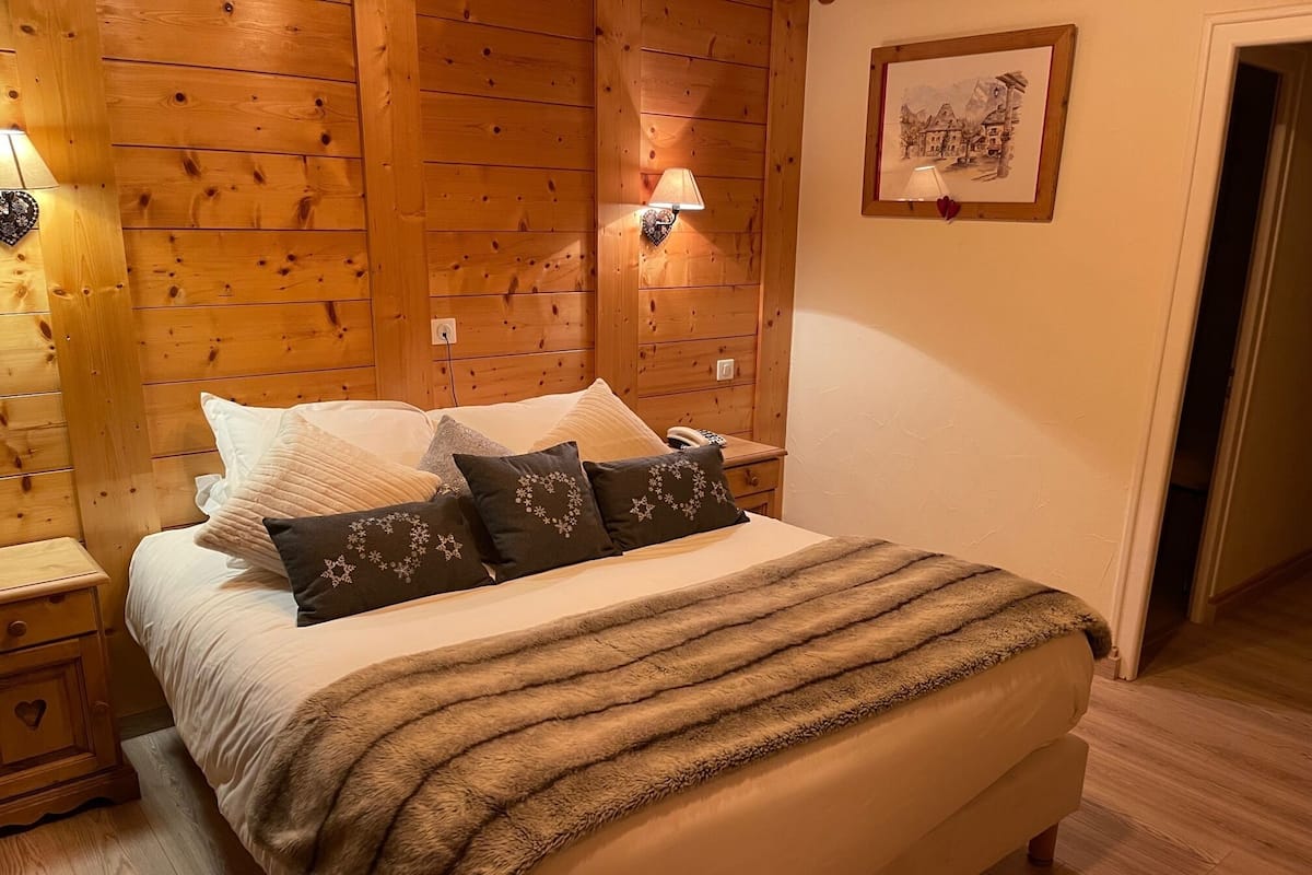 A wooden-paneled bedroom with a bed, pillows, a nightstand, a lamp, and a framed picture on the wall.