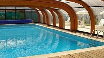 An indoor swimming pool with a wooden deck and a glass ceiling.
