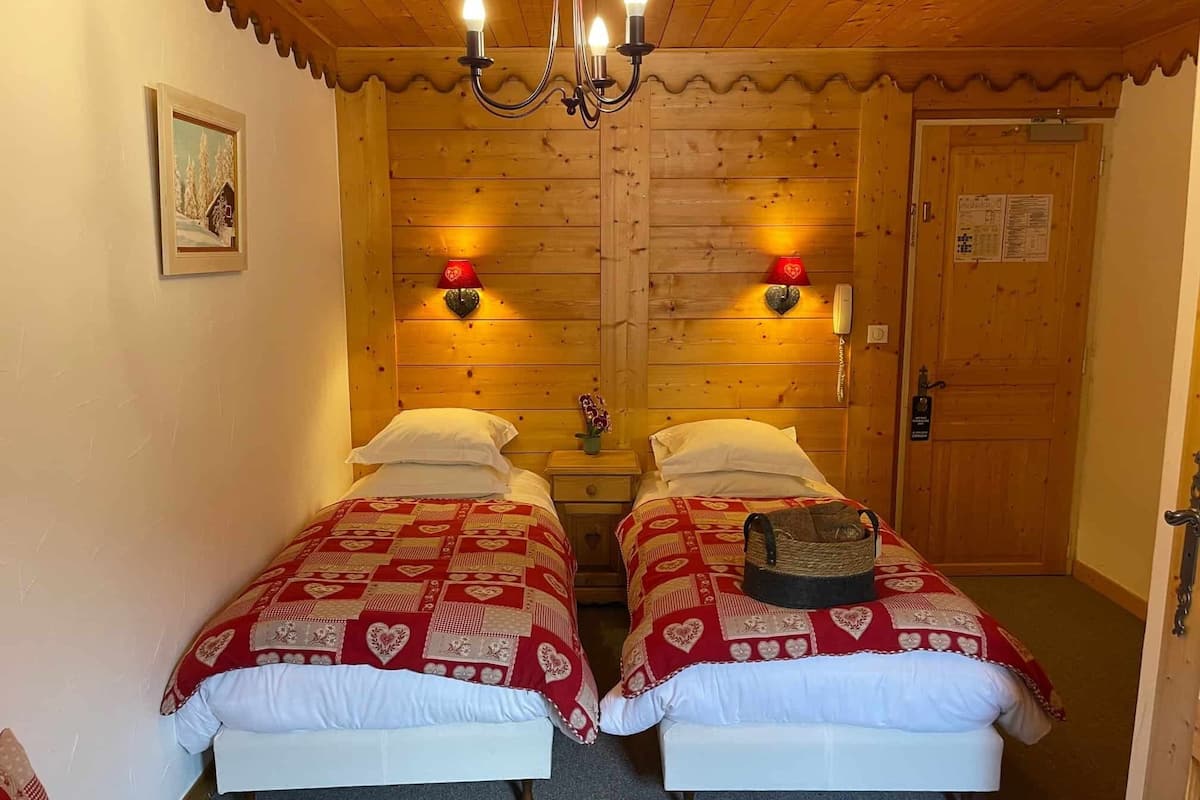 A room with two beds, each with a red heart-patterned bedspread, a chandelier, and a wooden door.