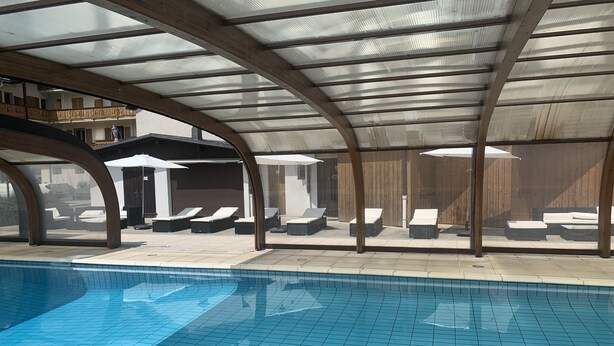 An indoor swimming pool with tiled walls and ceiling, surrounded by lounge chairs and umbrellas. - Hôtel les Glaciers (Samoëns)