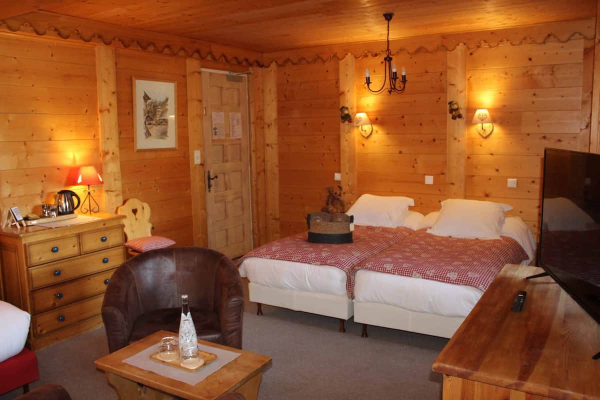 A wooden cabin room with a bed, a chair, a table, and a television.