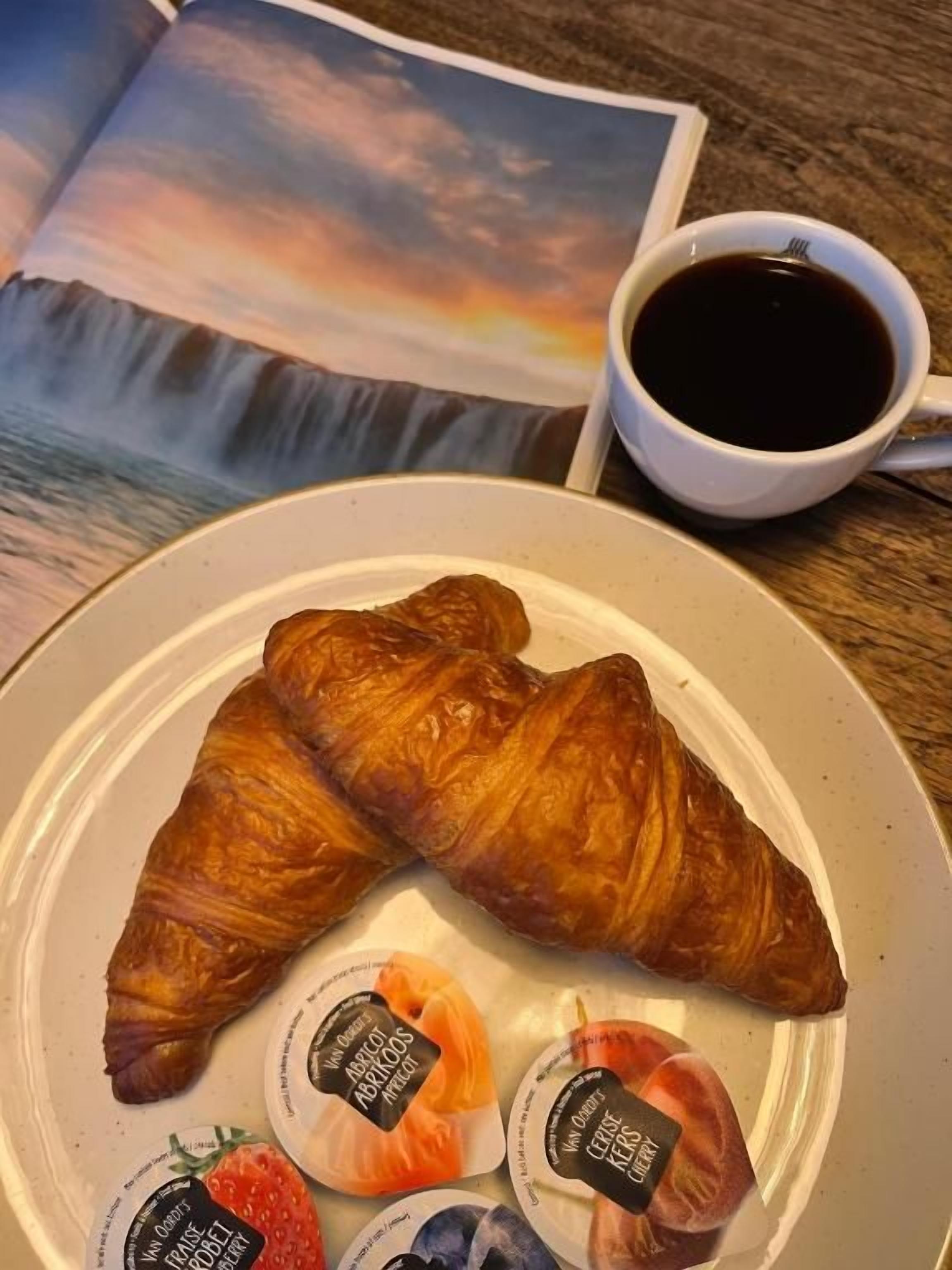 Ein Teller mit zwei Croissants, drei Joghurtbechern, einer Kaffeetasse und einer Zeitschrift mit einer Strandansicht.