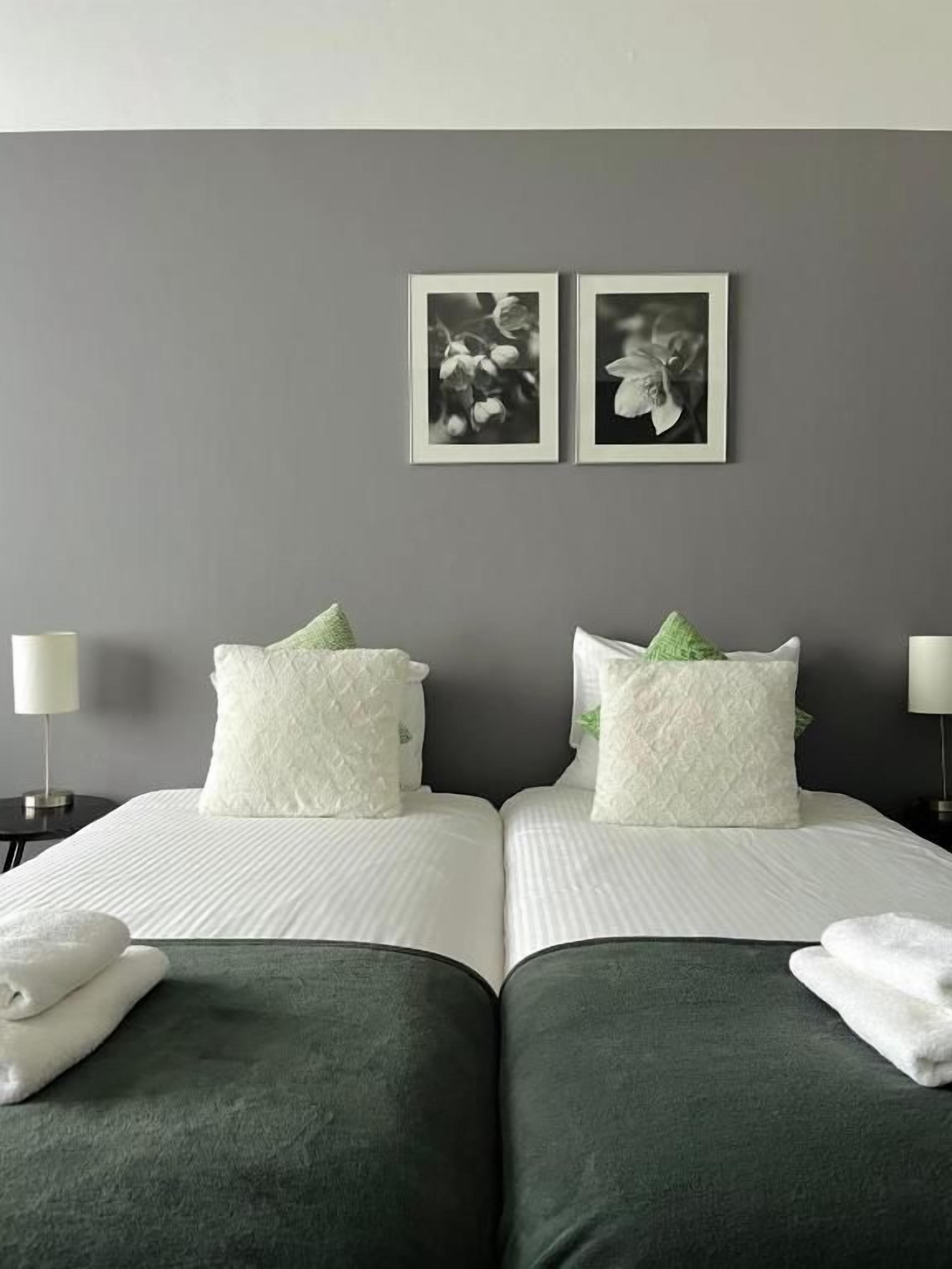 Een hotelkamer met twee bedden, een grijze muur en twee ingelijste foto's.