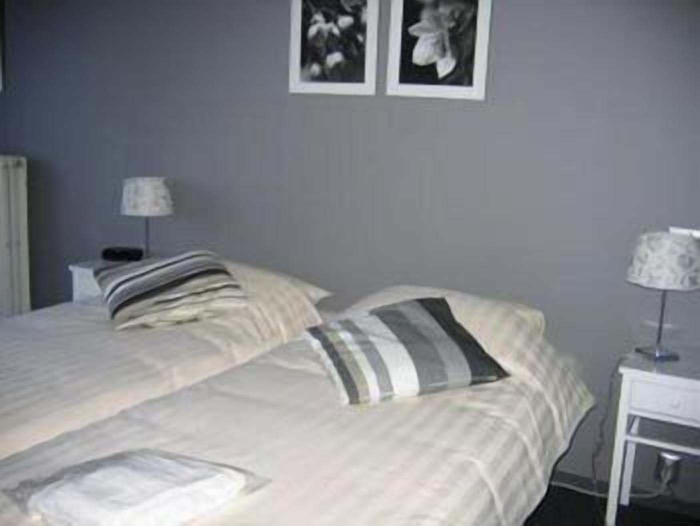 Un lit double avec une literie à rayures, une table de chevet avec une lampe et un cadre photo fixé au mur.