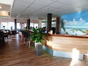Un área de bar con suelo de madera, una barra con un mural de una playa y varias sillas.