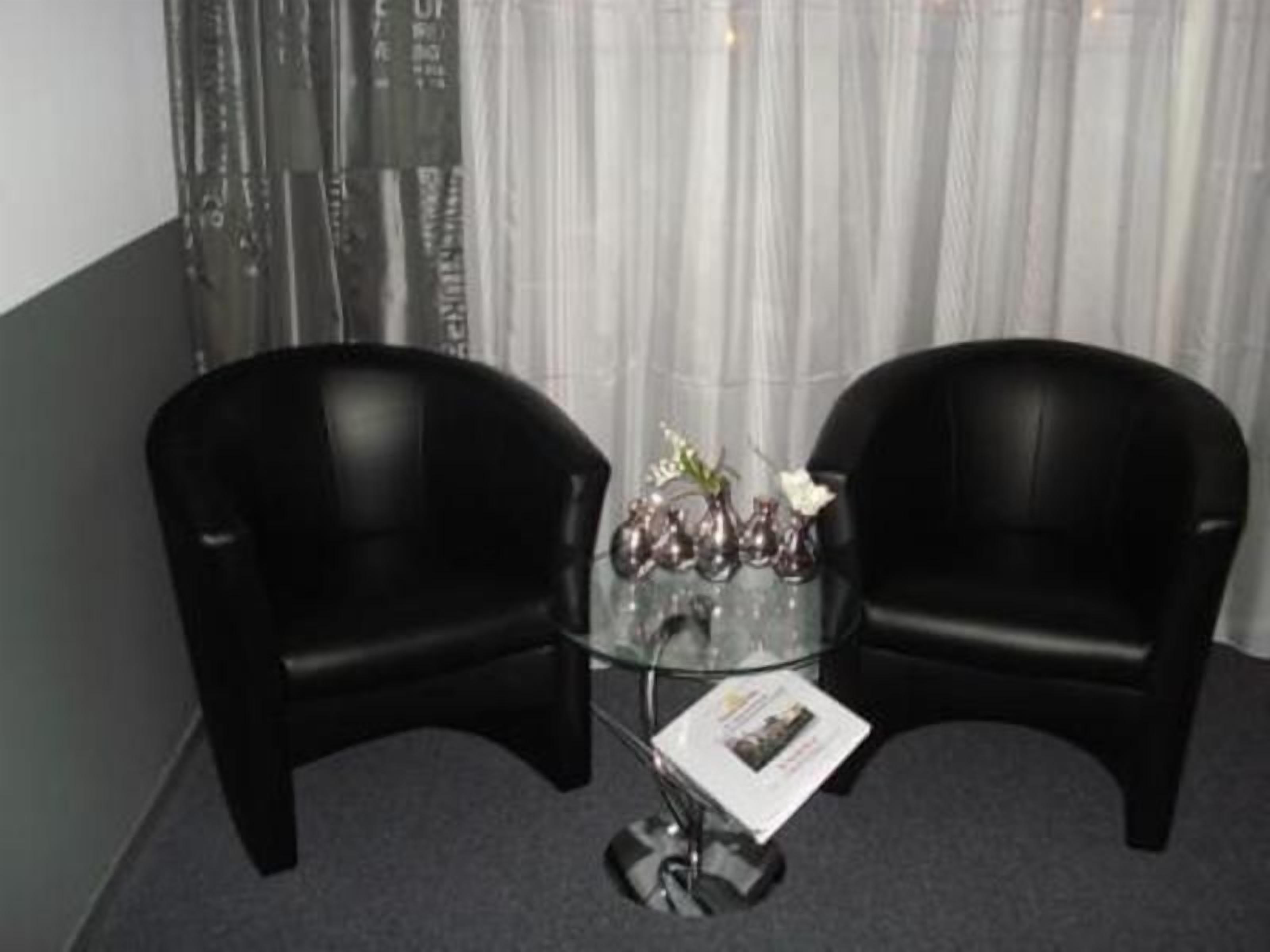 Two black leather chairs facing each other around a glass table with a vase of flowers and a magazine.