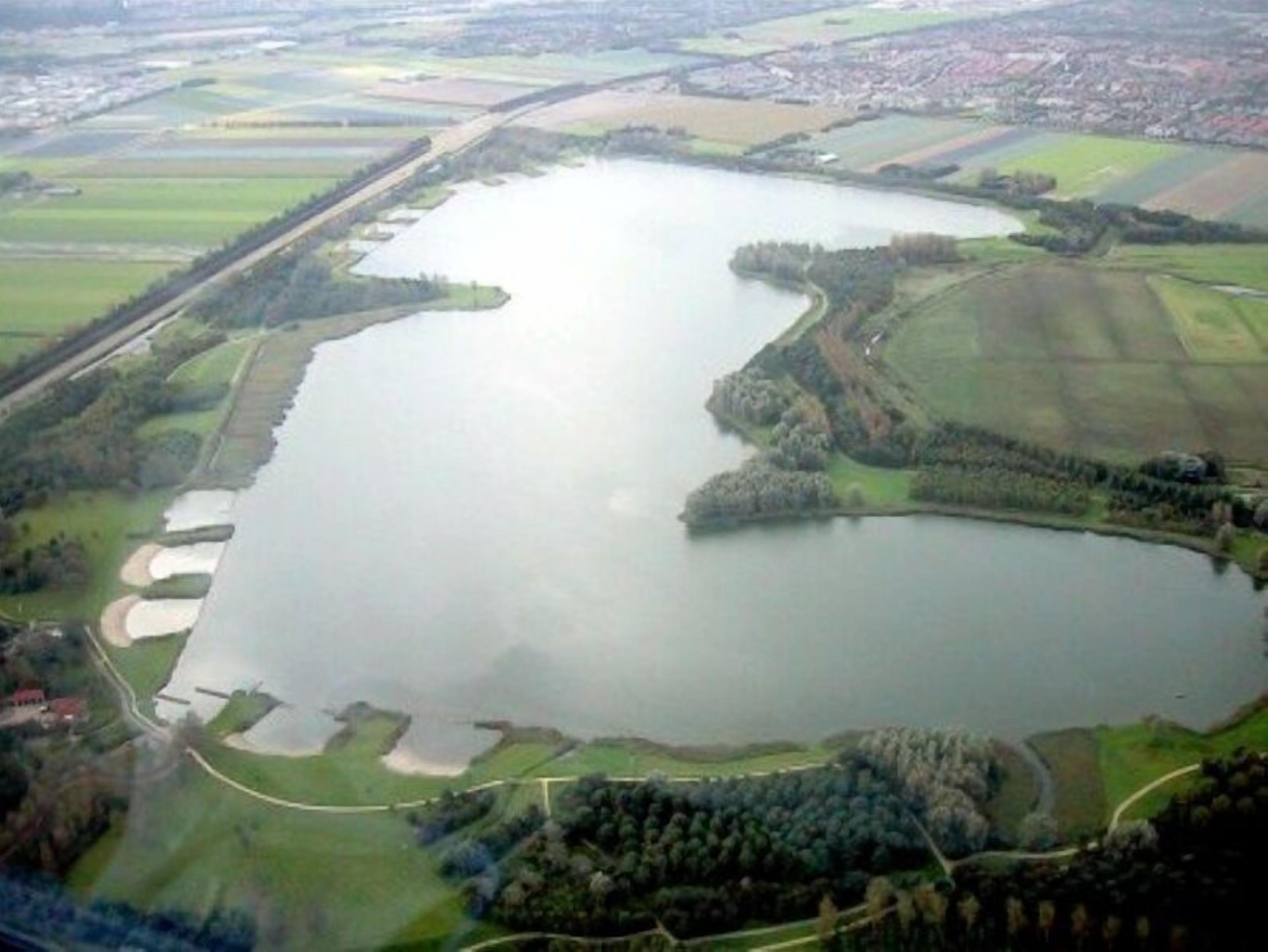 Vista aérea de un lago grande rodeado de campos verdes y algunos edificios.