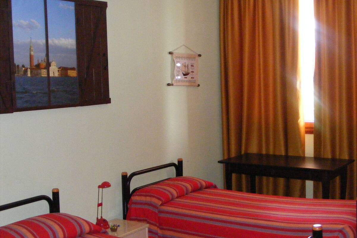 A bedroom with two beds, a small table, a nightstand, and a wall-mounted clock.