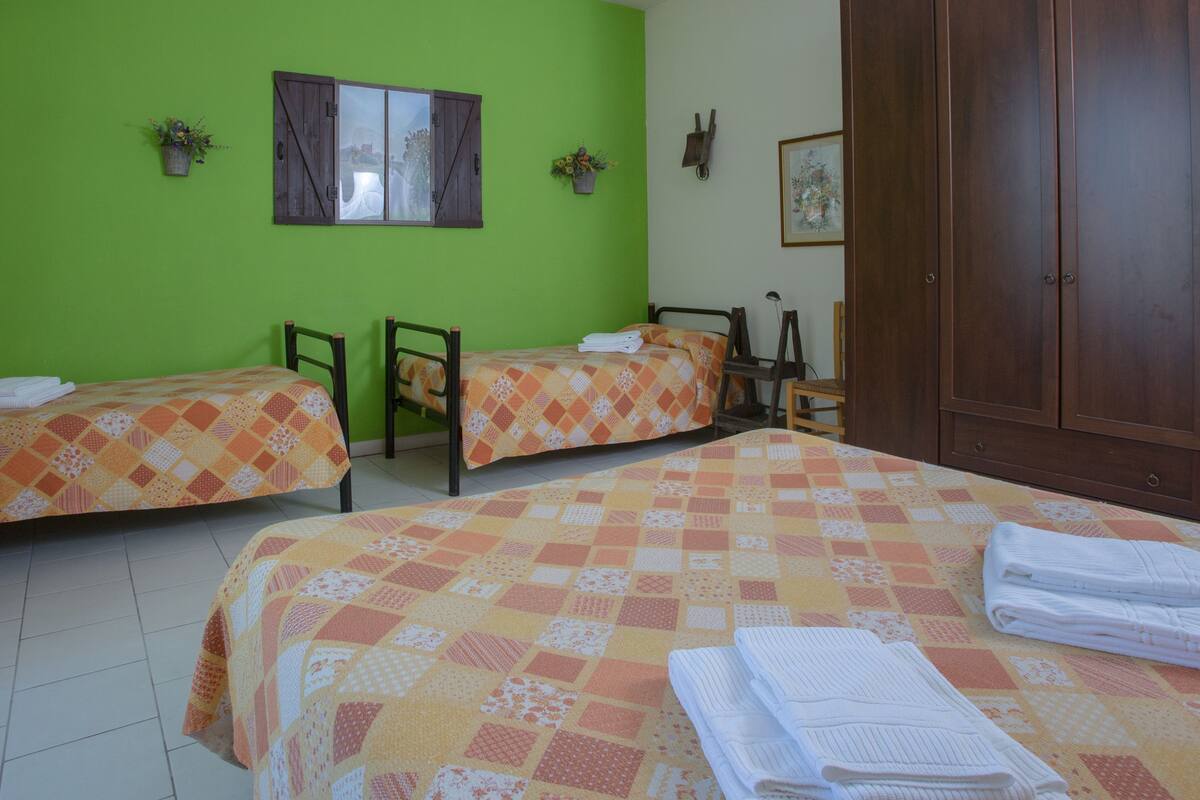 A room with two beds, a table, and a chair. There are two potted plants on the walls.