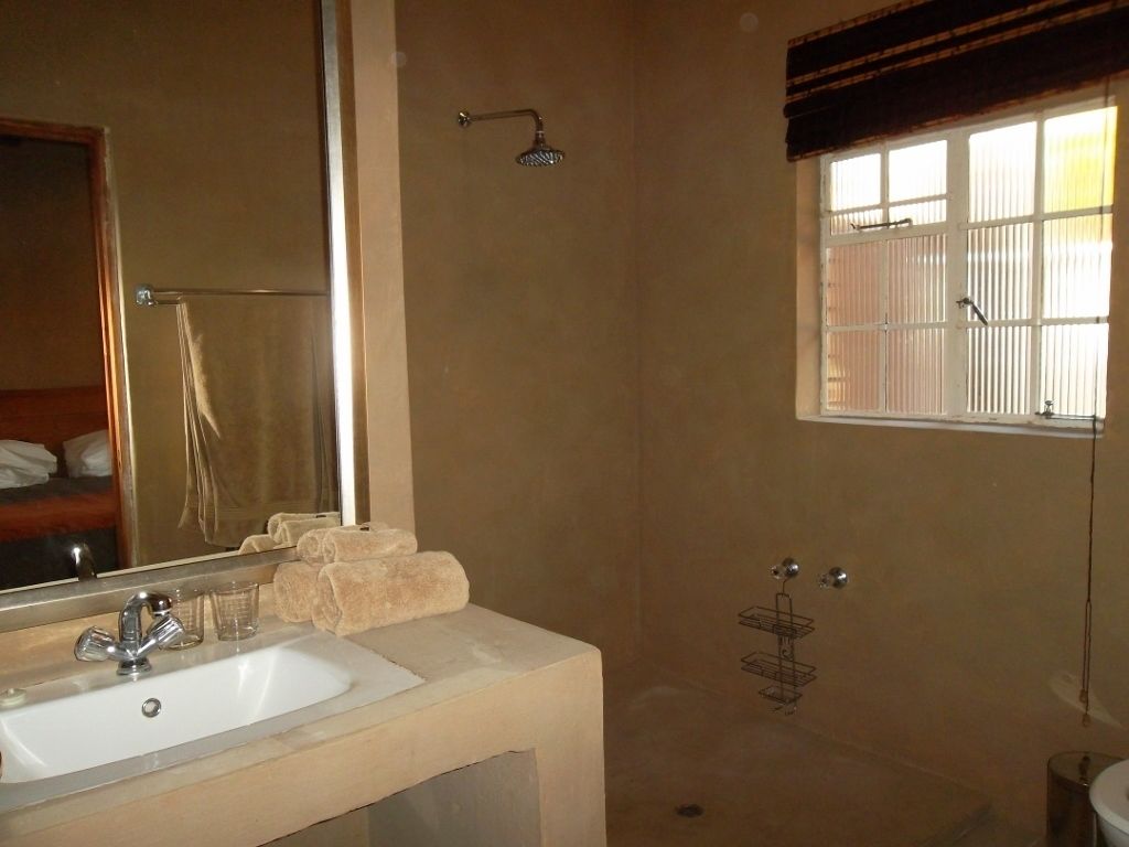 A bathroom with a sink, mirror, towel rack, shower, and window.