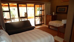 Een slaapkamer met een groot bed, een bank, een bureau en een stoel. Er is een schuifdeur die leidt naar een buitenruimte.