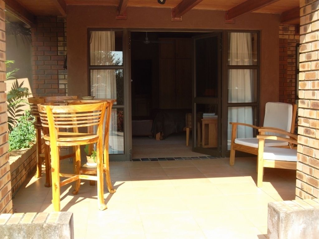 An outdoor patio area with a wooden table and chairs, a brick wall, and a sliding glass door leading to an interior space.