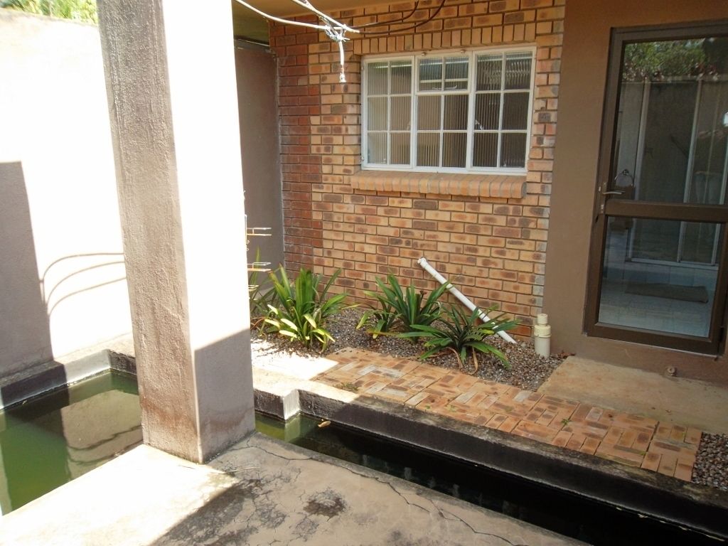 A residential property with a brick exterior, a window, a door, and a small garden area with plants.