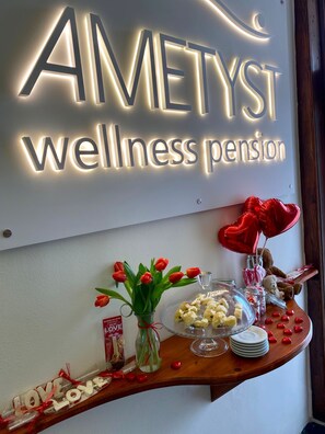 Une enseigne indiquant « AMETYST, maison de retraite axée sur le bien-être », avec une table où sont disposés des tulipes rouges, un bocal de chocolats et une assiette de pâtisseries.