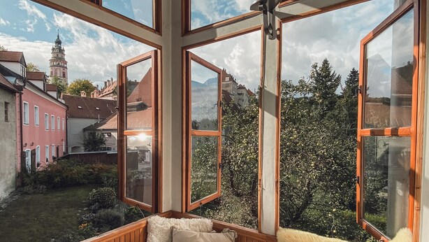 A cozy room with wooden walls and large windows, offering a view of a town with historic buildings and a church tower. - Boutique Pension Ametyst (Cesky Krumlov)