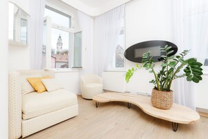Una sala moderna con sofá, una silla pequeña, una mesita de centro curvada y una planta en maceta.