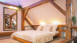 A bedroom with a wooden bed frame, a large mirror, and a staircase with wooden beams. - Boutique Pension Ametyst (Cesky Krumlov)