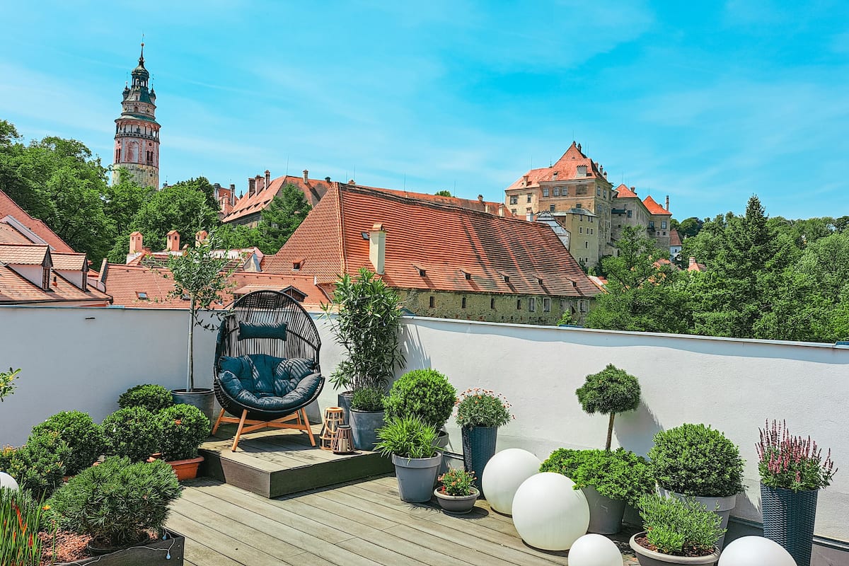 A rooftop garden with potted plants, a unique chair, and a view of historic buildings.