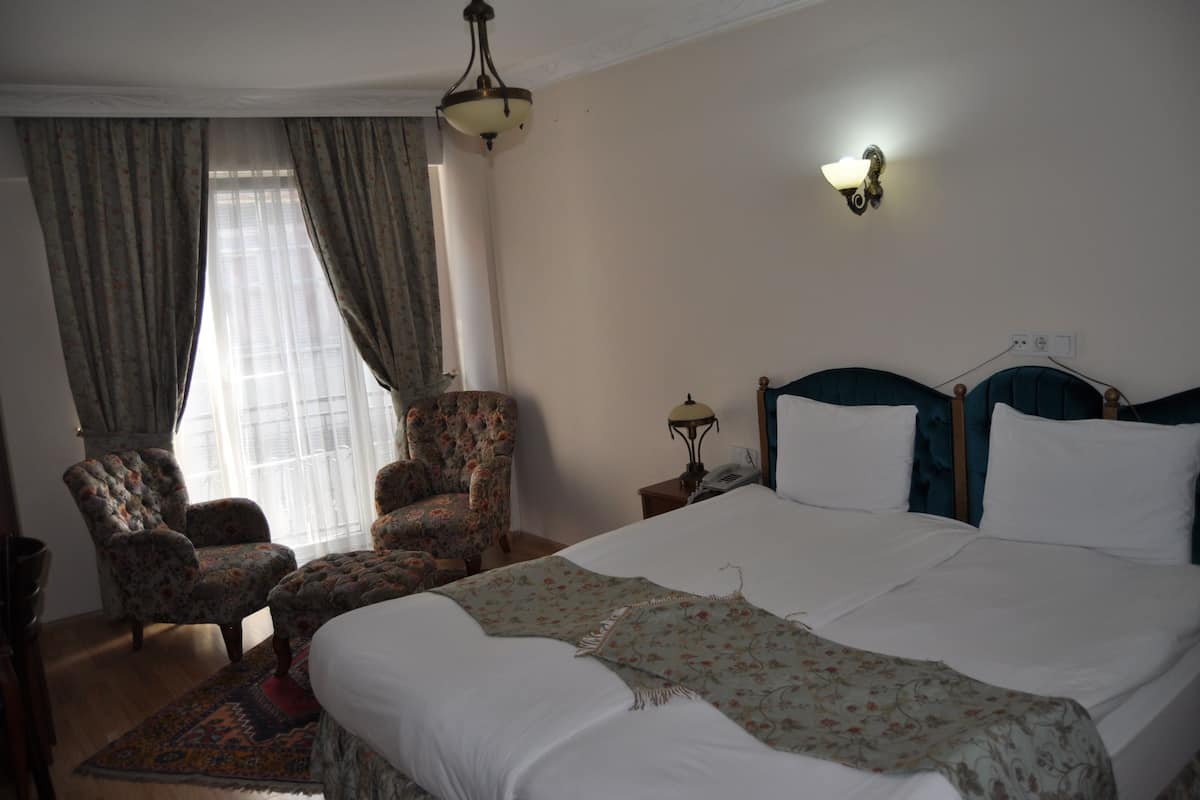 A hotel room with a large bed, two armchairs, a nightstand, and a lamp.