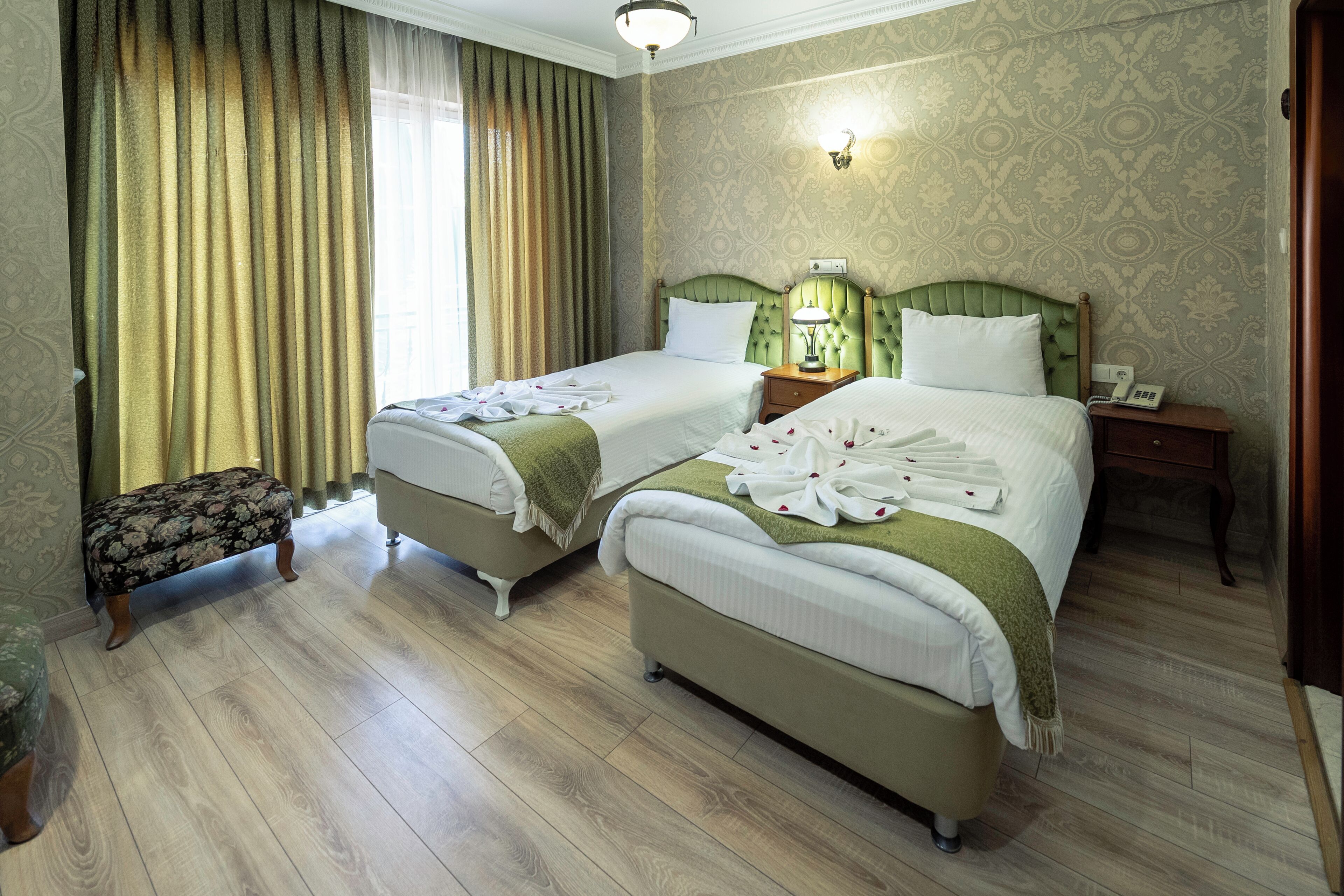A hotel room with two beds, a small bench, and a nightstand with a lamp.