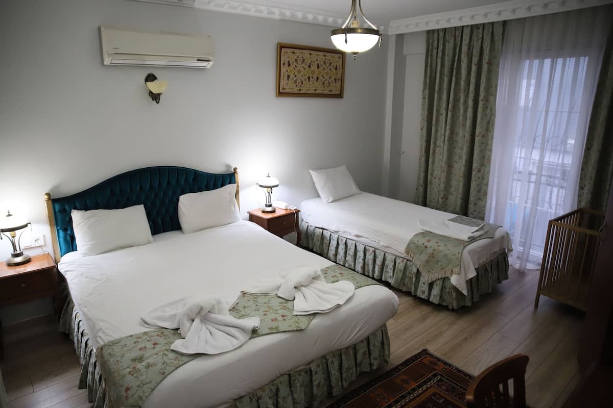 A hotel room with two beds, a nightstand, a lamp, an air conditioner, a decorative wall piece, and a crib.