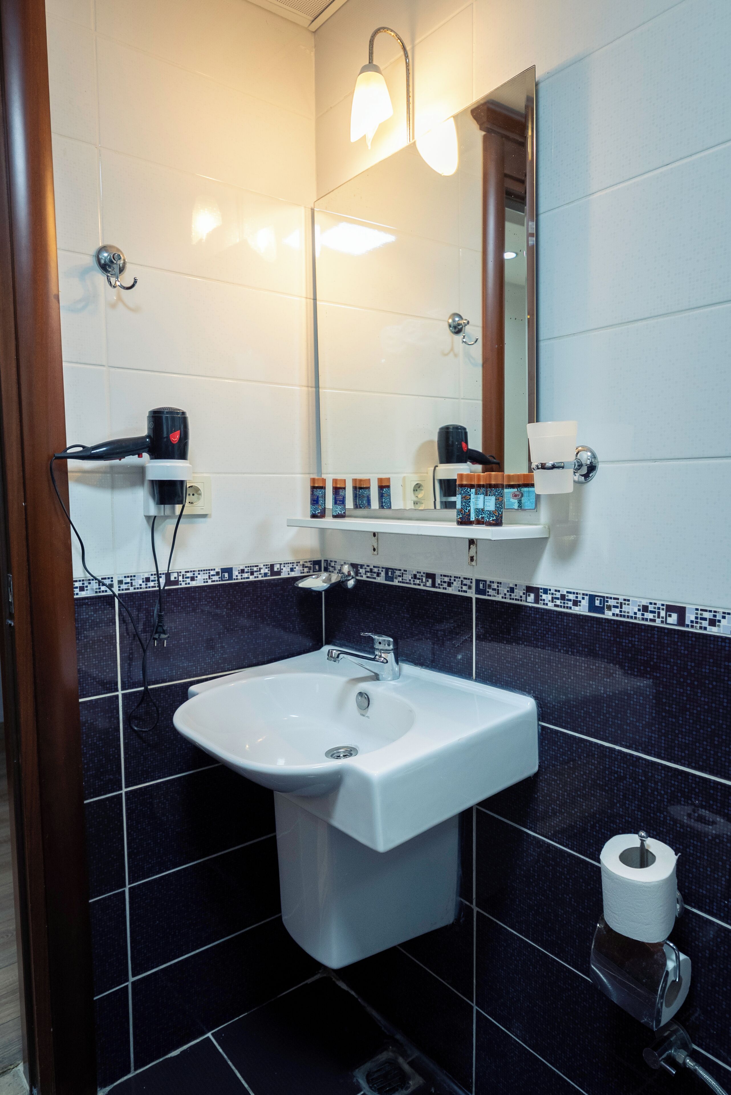 Un baño con lavamanos blanco, un espejo, un secador de pelo y un estante con artículos de aseo.