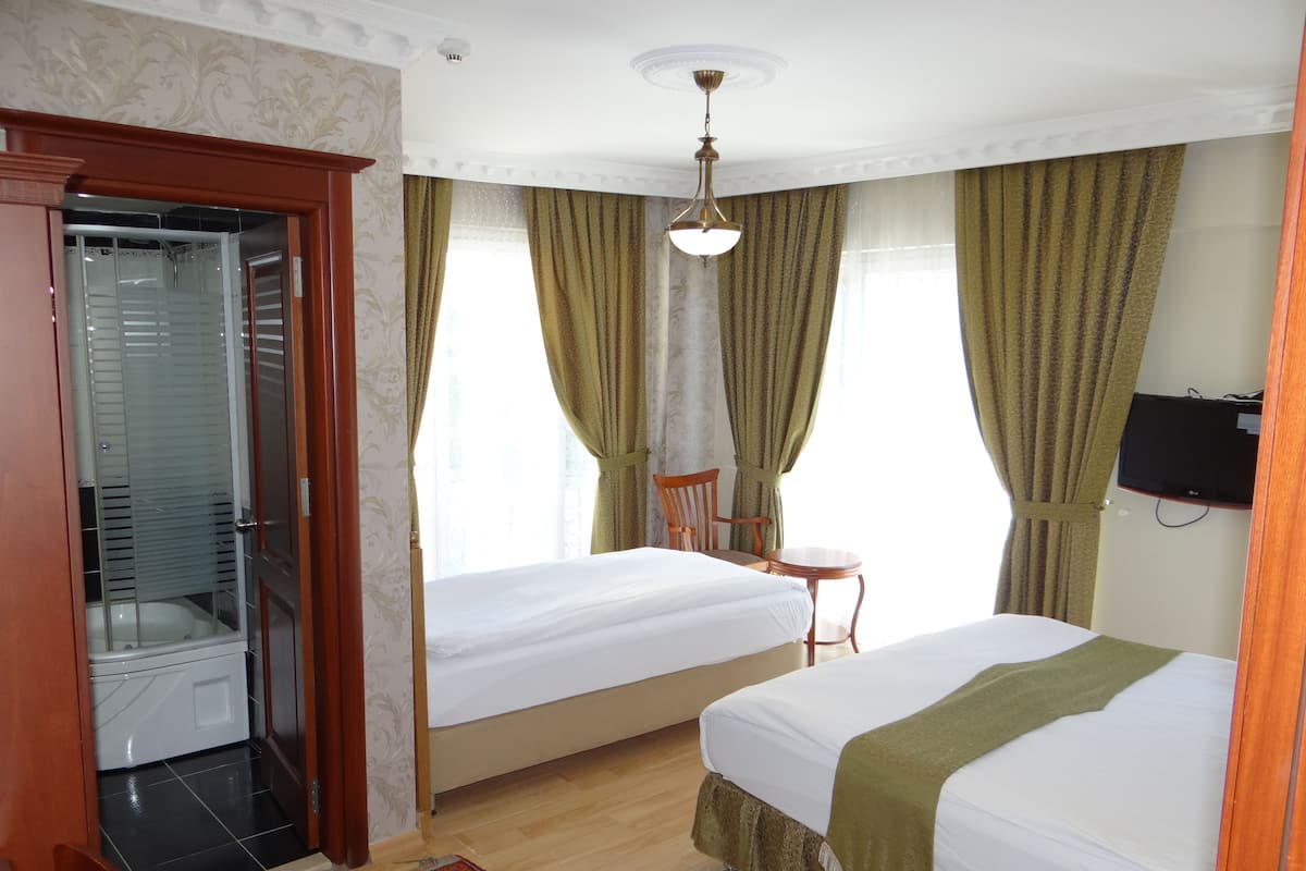 A hotel room with two beds, a shower, a chair, a small table, and a TV mounted on the wall.