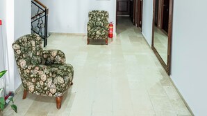 Ein geräumiger Raum mit hoher Decke, einem armchair mit floralem Muster, einem Feuerlöscher und einer Tür zu einem weiteren Bereich.