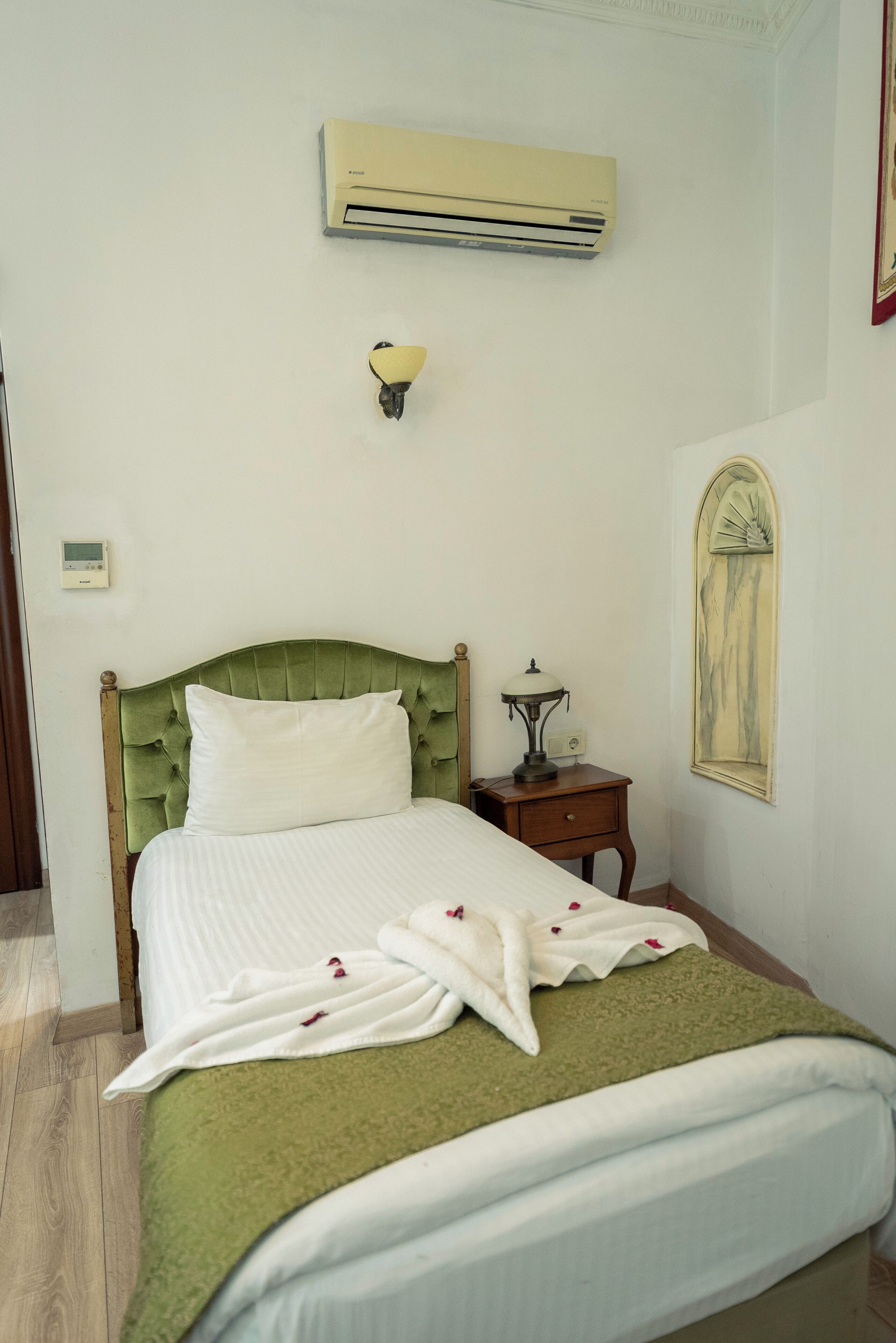 A neatly made bed with a green headboard, a bedside table with a lamp, and an air conditioning unit on the wall.