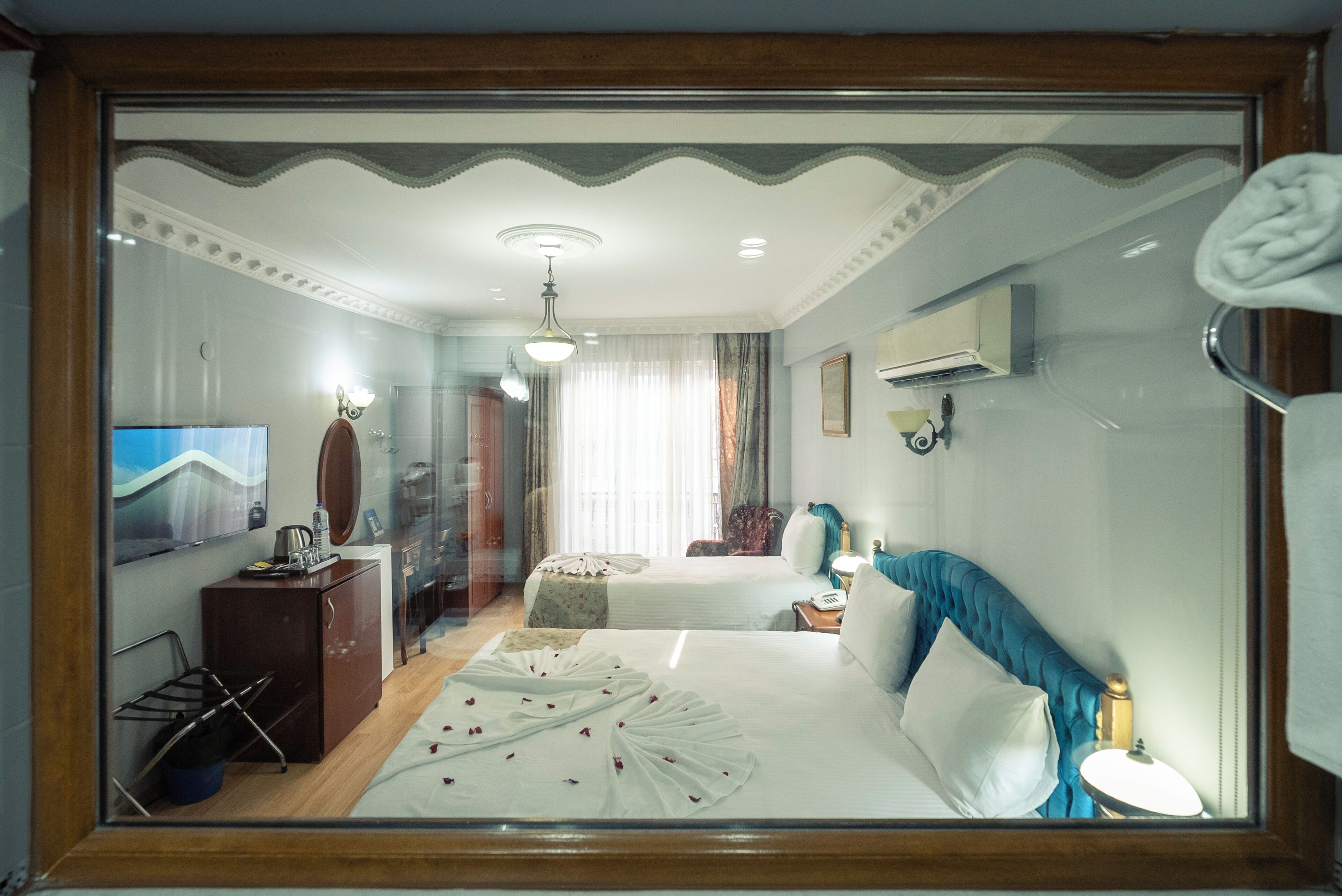 A hotel room with two beds, a television, a desk with a telephone, and a mirror.
