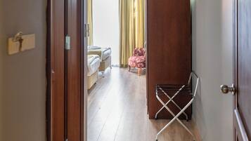 A hotel corridor with a wooden floor, a bed, a chair, and a wardrobe.