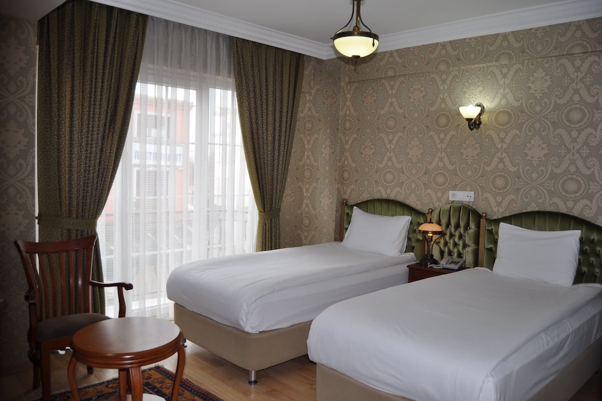 A hotel room with two beds, a chair, a small table, and a nightstand with a lamp.