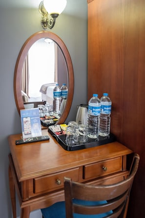 A hotel room with a wooden desk, a mirror, a tray with water bottles, a remote control, and a minibar. - Basileus Hotel (Istanbul)