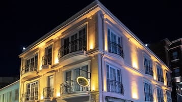 Un hôtel à plusieurs étages doté d’un balcon au deuxième étage, d’une entrée au rez-de-chaussée avec une porte et d’une enseigne indiquant le nom de l’hôtel.