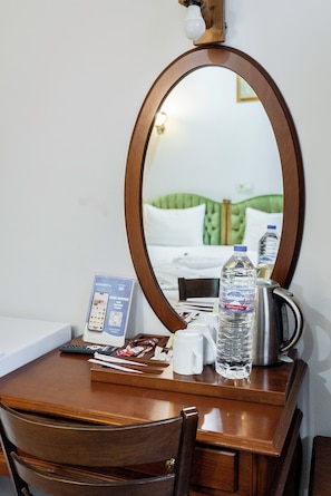 A hotel room with a wooden desk, a mirror, a telephone, a water bottle, a kettle, and a bed with green bedding. - Basileus Hotel (Istanbul)
