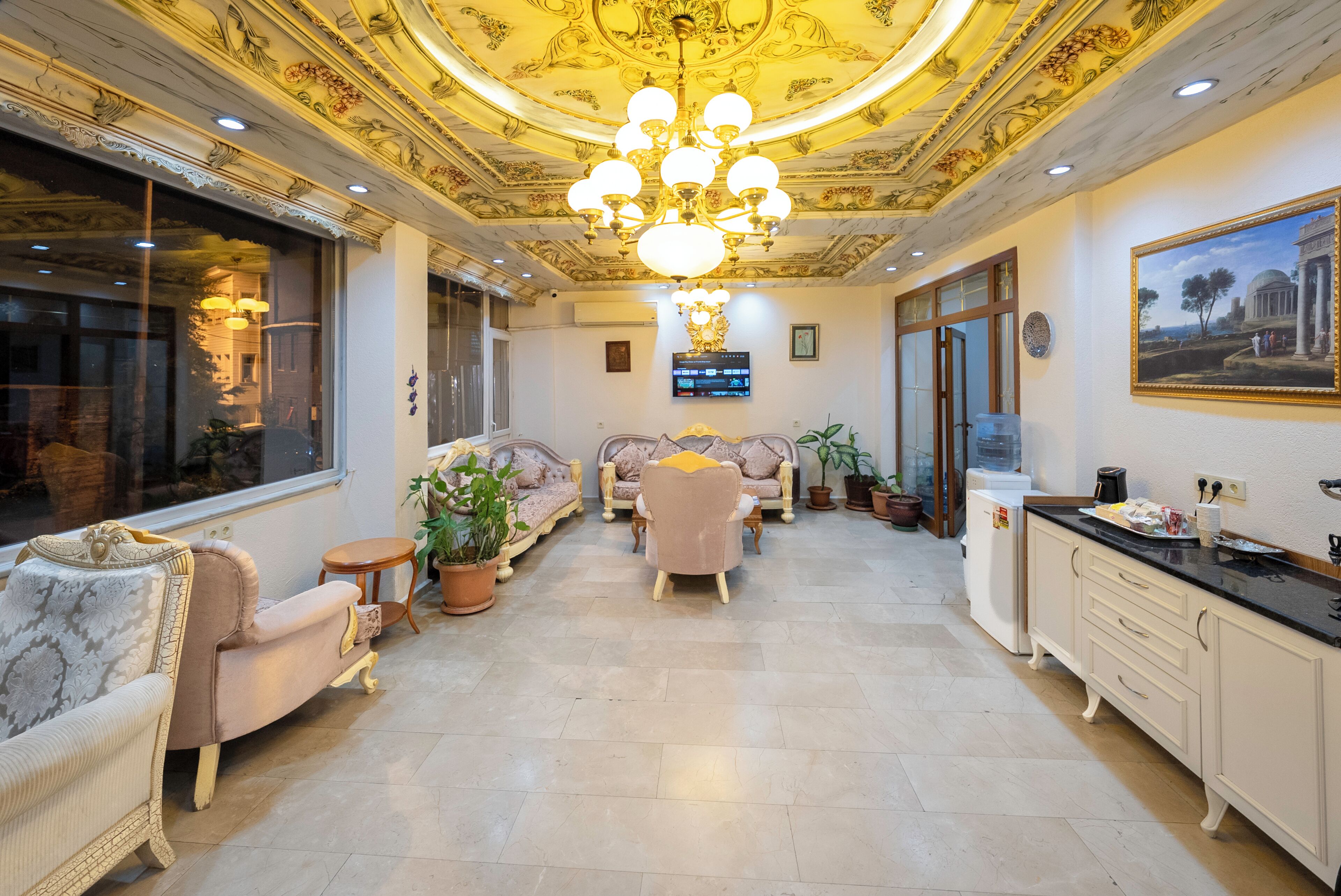 Ein geräumiger Wohnbereich mit einer Chandelier, Sofas, einem Fernseher und einem Gemälde an der Wand.