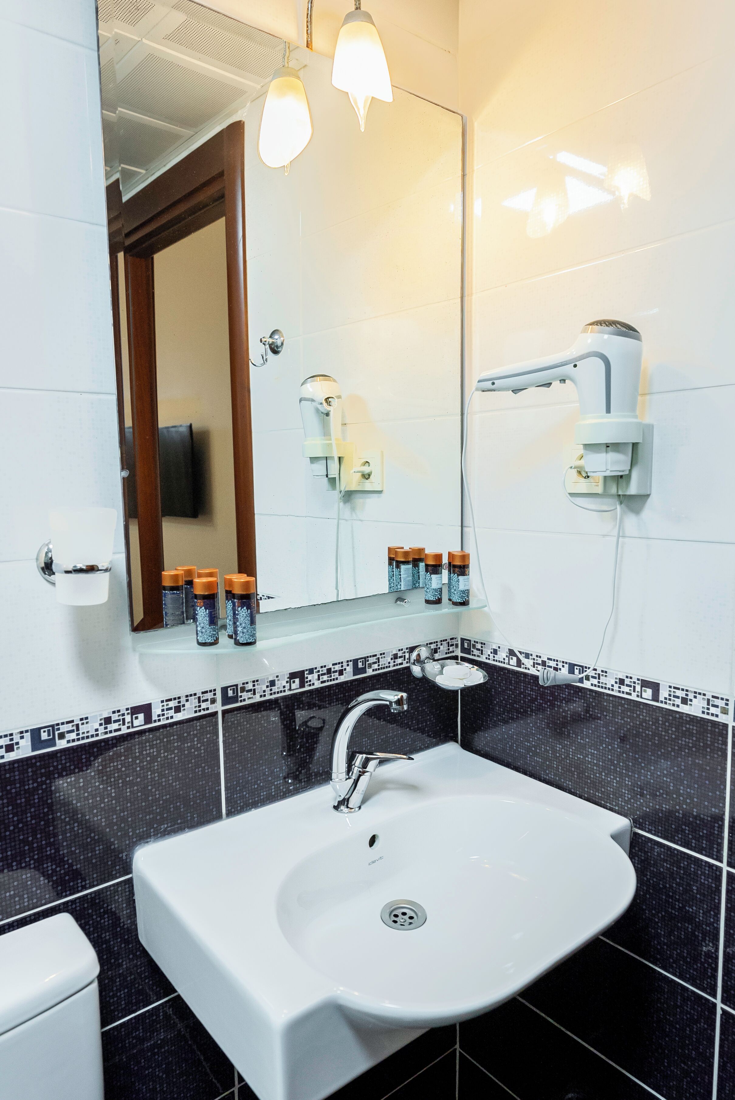 A bathroom with a white sink, a mirror, and a shower. There are toiletries on the sink and a towel rack on the wall.