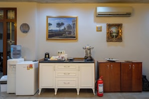 Una cocina equipada con refrigerador, dispensador de agua, cafetera, licuadora y extintor.
