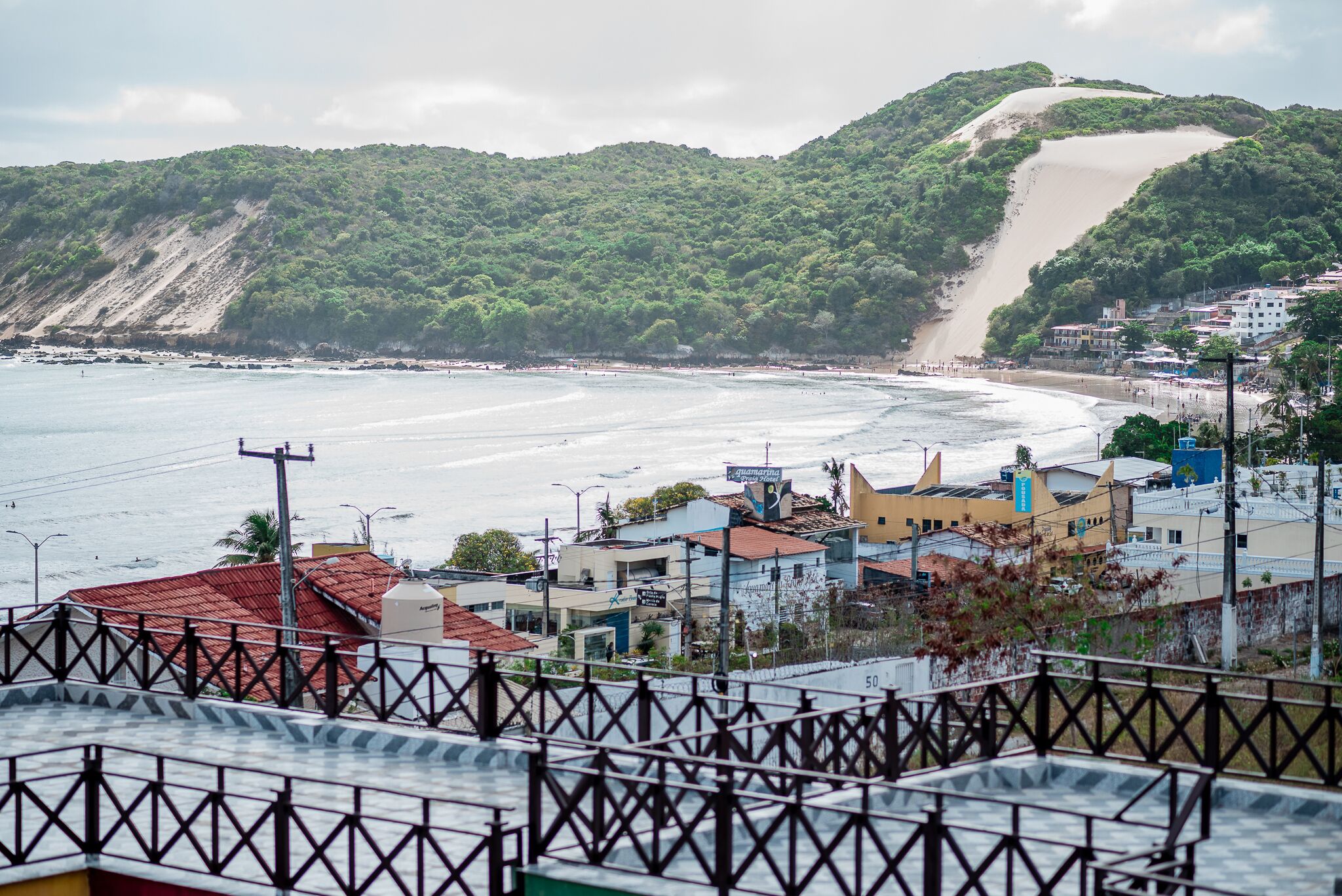A coastal town with buildings near the beach, a prominent hill, and a clear view of the sea.
