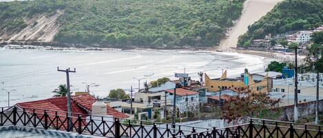 A coastal town with buildings near the beach, a prominent hill, and a clear view of the sea.