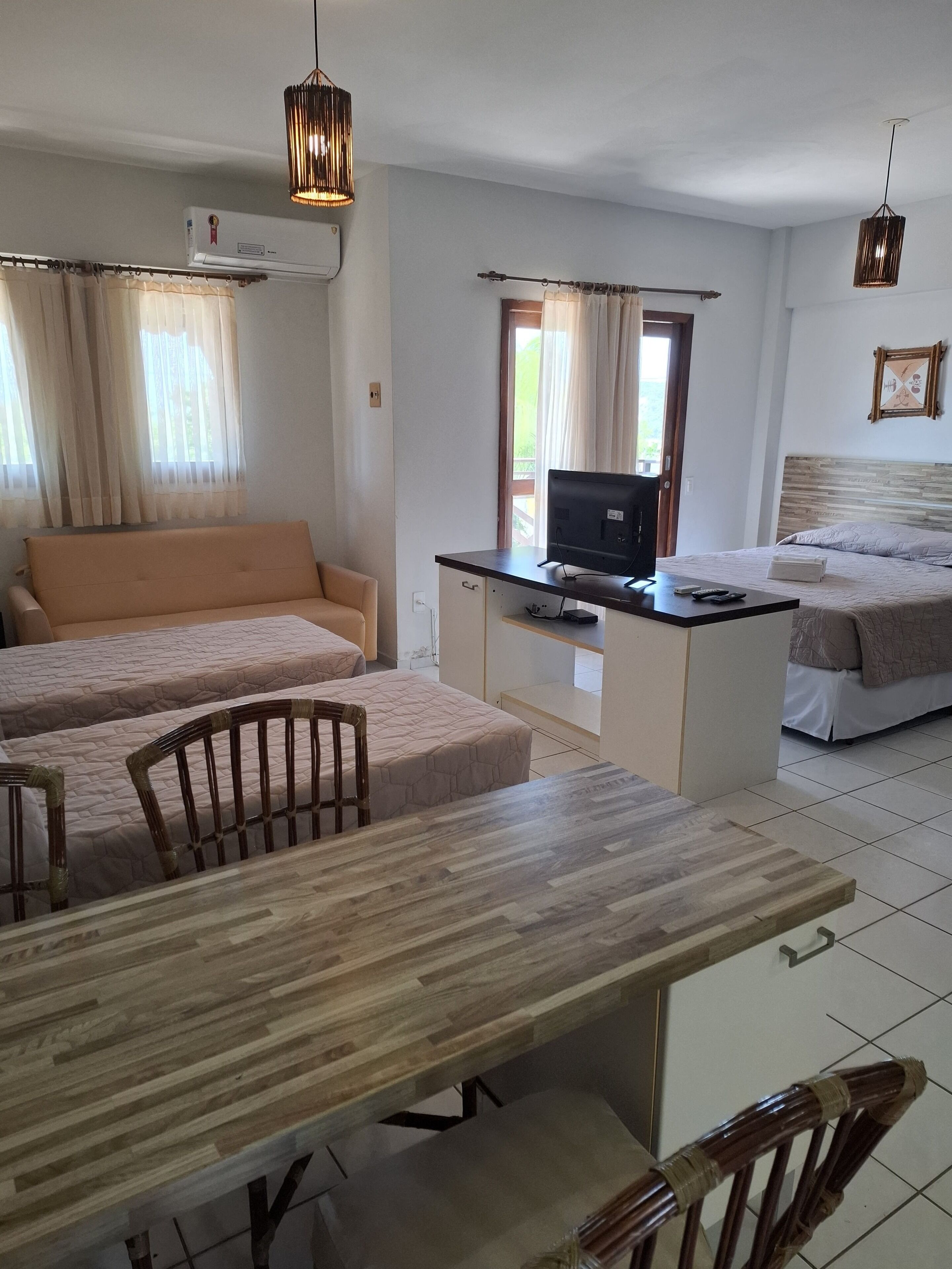 A hotel room with a wooden dining table, two single beds, a TV on a desk, and a window with curtains.