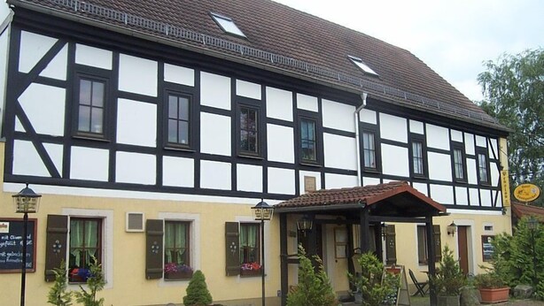 Un bâtiment traditionnel à colombages, doté d’une entrée couverte et de plantes en pot devant la façade.